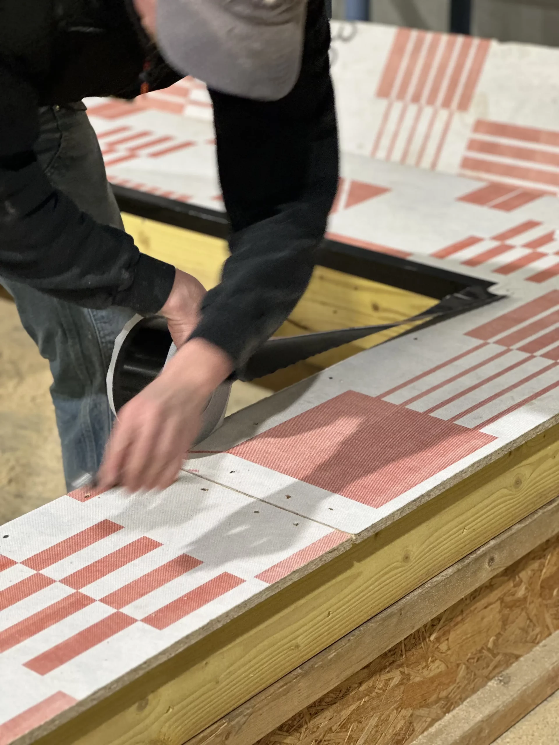 Homme en train d'appliquer l'adhésif Bardane Uv Easy Nuuk® sur le panneau de contreventement pare-pluie Bau ExWall® 1000